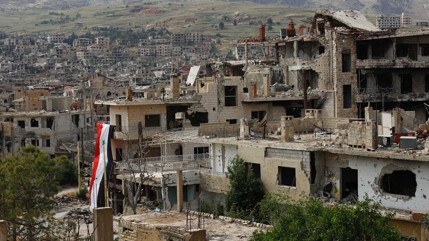 A huge Syrian National flag hangs out of a damage building.