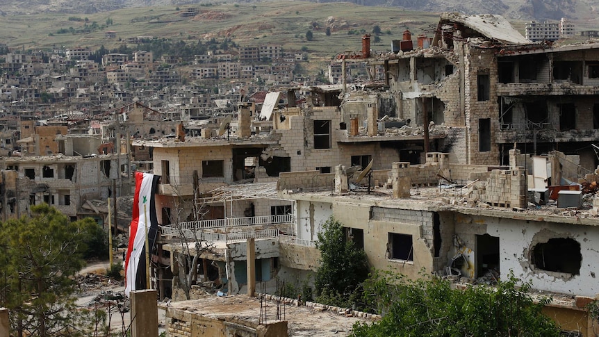 A huge Syrian National flag hangs out of a damage building.