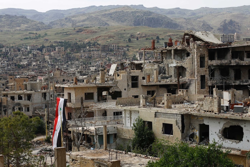 A huge Syrian National flag hangs out of a damage building.