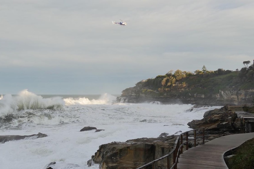 A helicopter hovers over Bondi Beach with rough swell