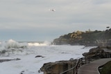 A helicopter hovers over Bondi Beach with rough swell.