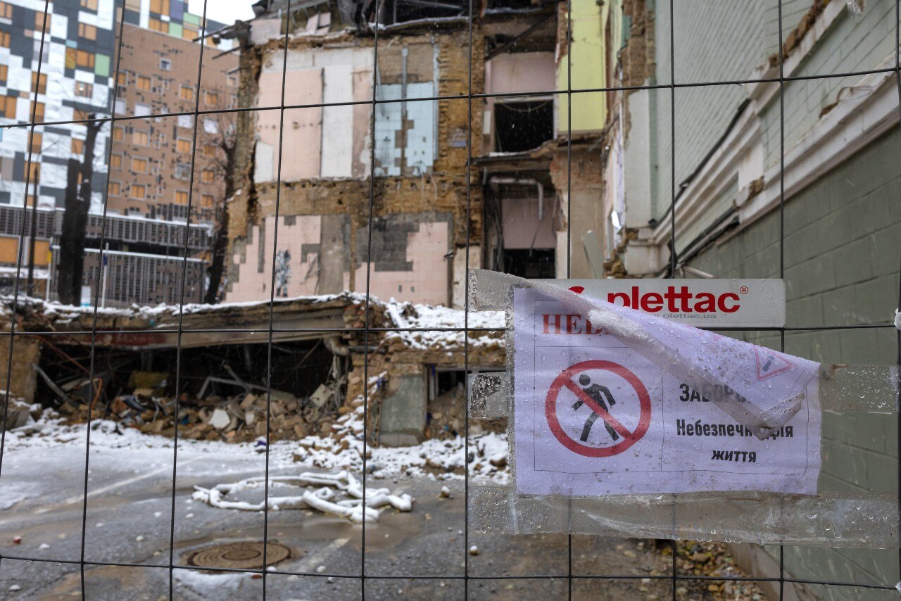 The exterior of a damaged building, seen through a wire fence.