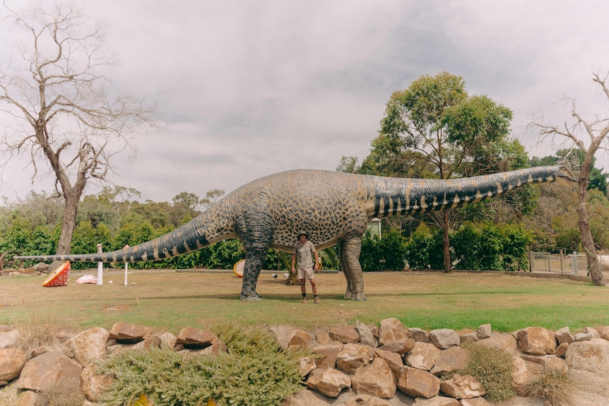 a man stands in front of a large dinosaur replica