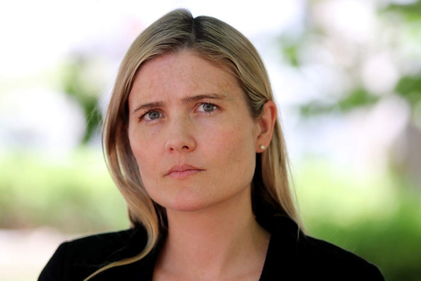 A close up of Sophie with shoulder-length blonde hair, wearing a black blazer looking directly at the camera.