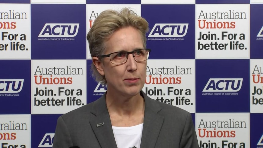 A woman with grey mullet-style hair cut speaking at a media conference.