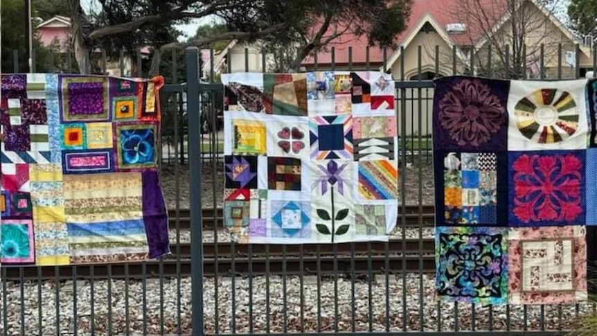 Three colourful square quilts hung on an iron fence