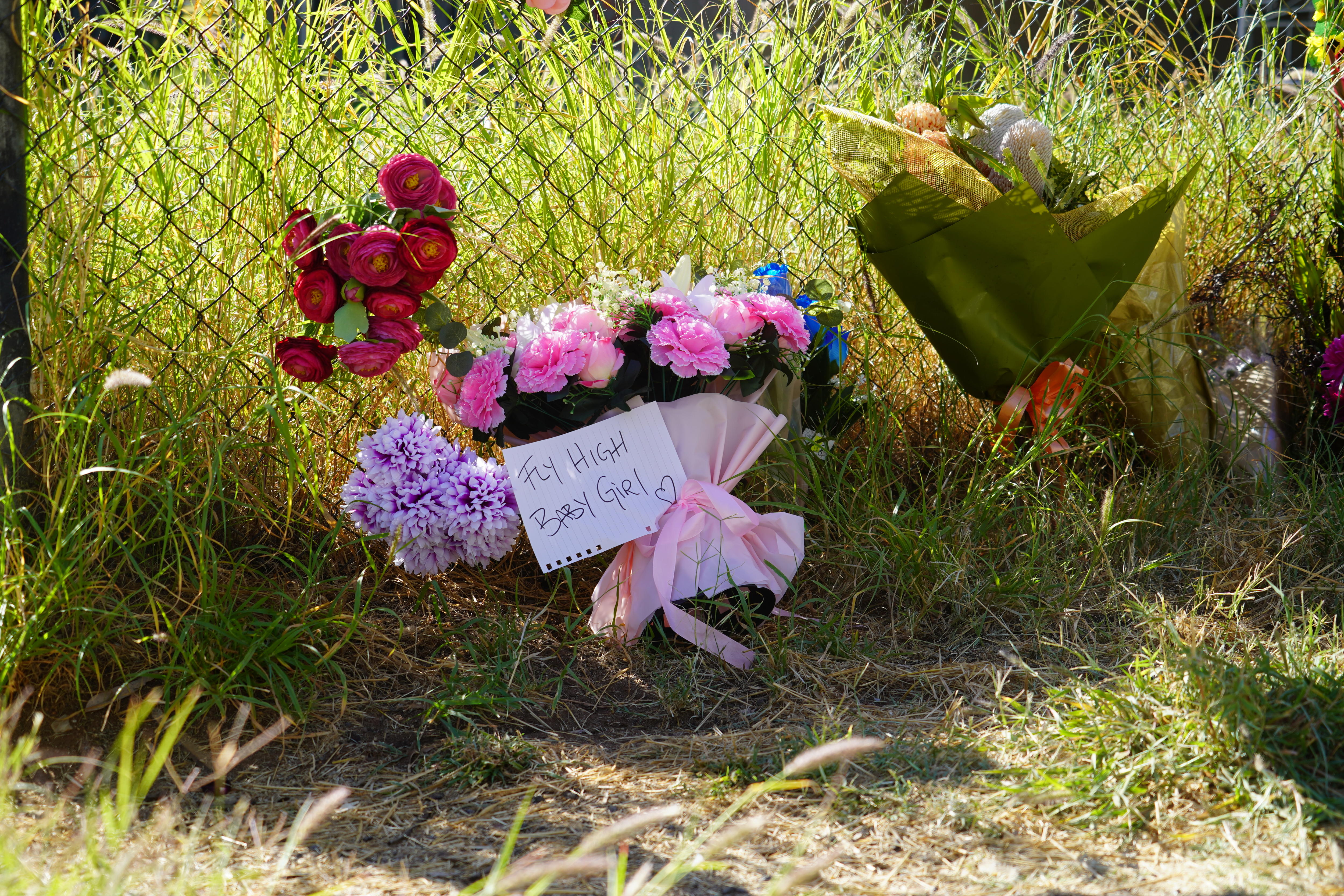 Flowers on a fence with a note reading fly high baby girl