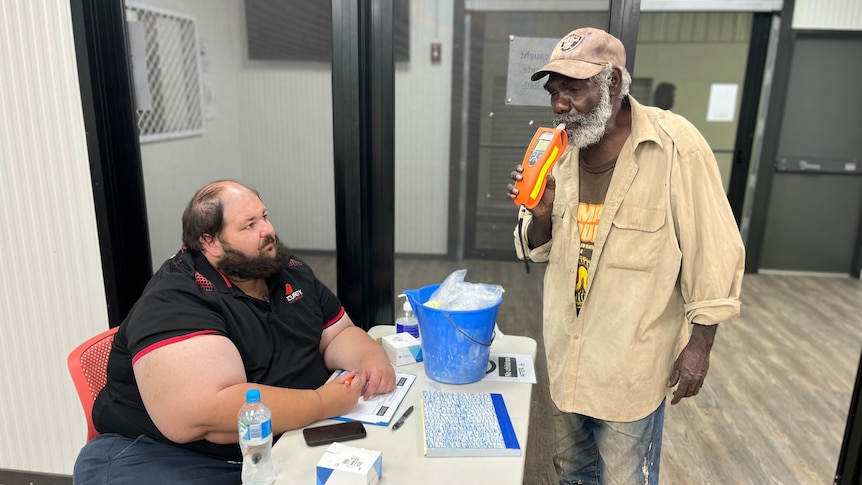 an aboriginal man wearing a cap is being breath-tested