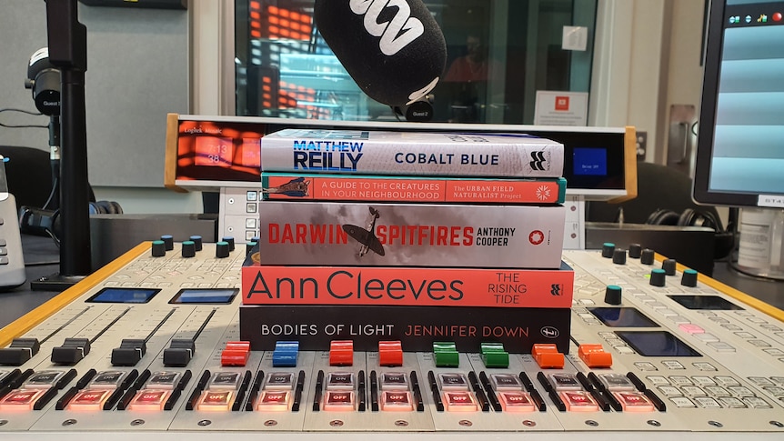 five books stacked on top of each other on a radio mixing desk with a microphone nearby
