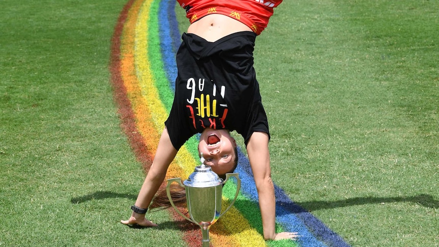 Jade Pregelj is upside down mid-cartwheel in front of a trophy. The 50m arc is painted in rainbow colours below here