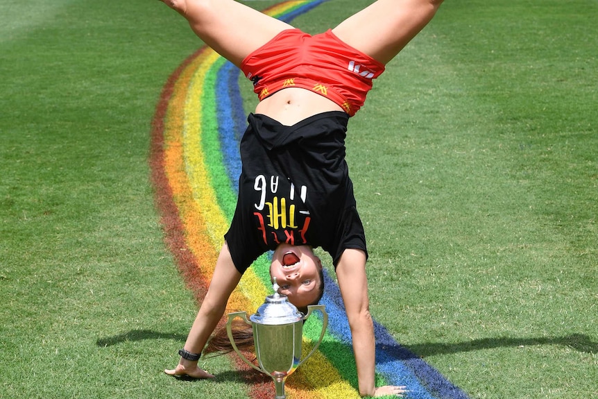 Jade Pregelj is upside down mid-cartwheel in front of a trophy. The 50m arc is painted in rainbow colours below here