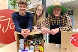 Tomas Dowler, Gemma Ritchie and Jordan Fitzgerald  lean on a box of food and smile at the camera