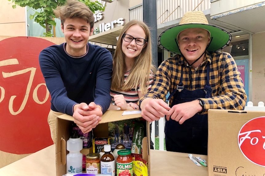 Tomas Dowler, Gemma Ritchie and Jordan Fitzgerald  lean on a box of food and smile at the camera