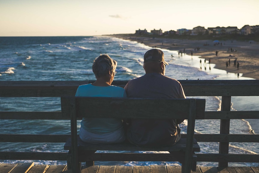 Couple sit on bench looking out at sea