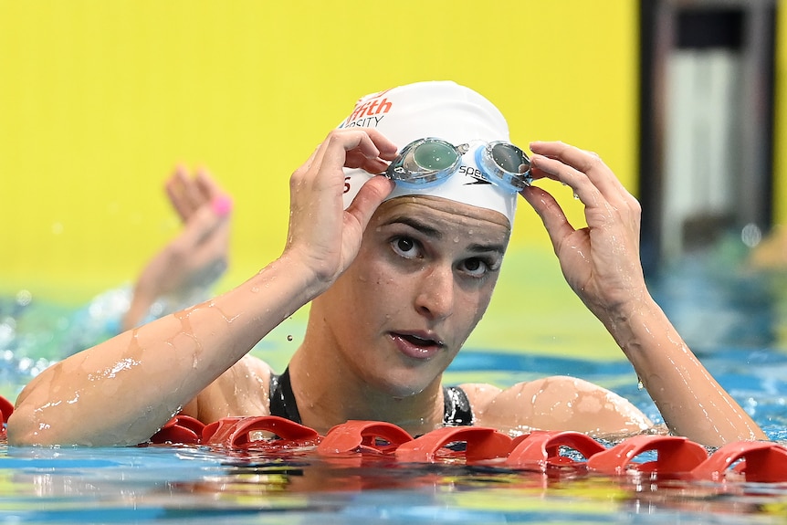 Kayley McKeown looks up and holds her goggles as she leans on a lane rope