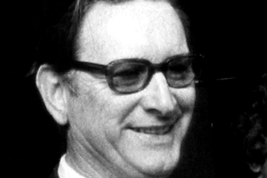 A black and white still of Jack Herbert. The image is a close-up of Herbert's face. He is wearing reading glasses.