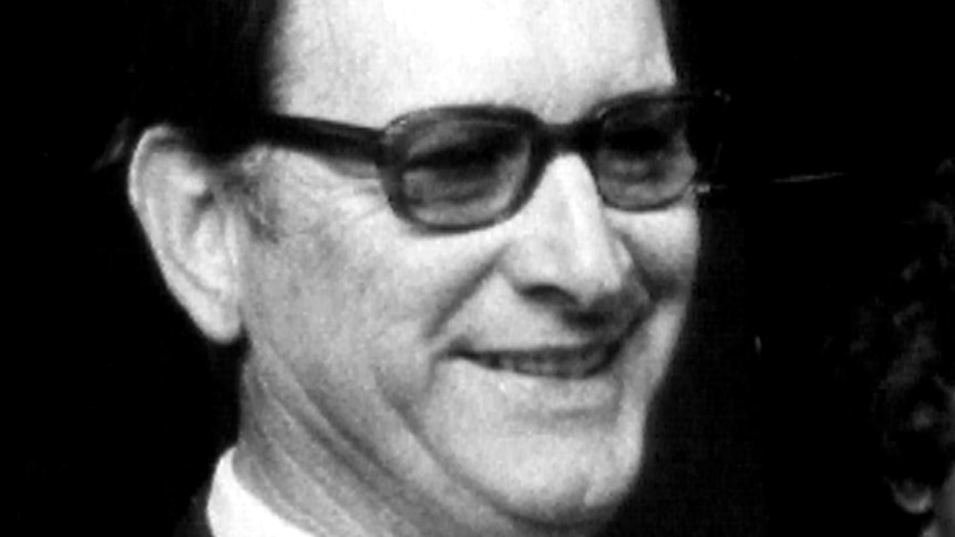 A black and white still of Jack Herbert. The image is a close-up of Herbert's face. He is wearing reading glasses.