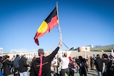 A group of protestors marching towards parliament house in Canberra, one waving an Aboriginal flag high.