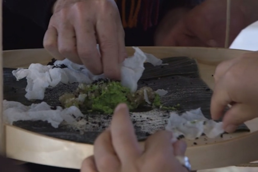 Hands dipping rice chips into dip containing ants