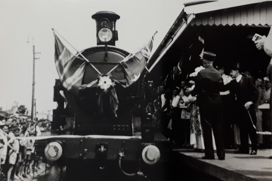 A black and white image of a train arriving at a station in 1913, with people standing on the platform