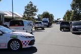 Two police cars parked on a suburban street. Police tape spans across the street.