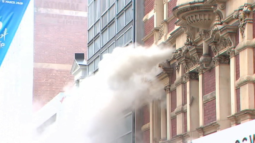 Smoke near a historic building with a festival sign in front and people watching