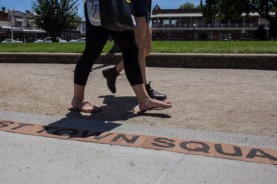 Two women's legs walking past paving stones saying town square