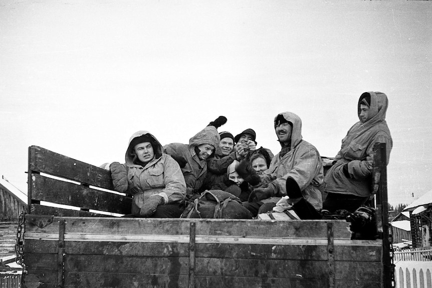 A black and white photo of a group of young people in hooded coats in the back of a ute