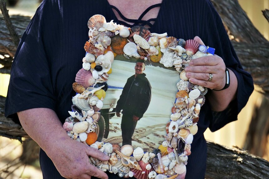 A picture frame containing a smiling photo of Damian Noakes on a beach.