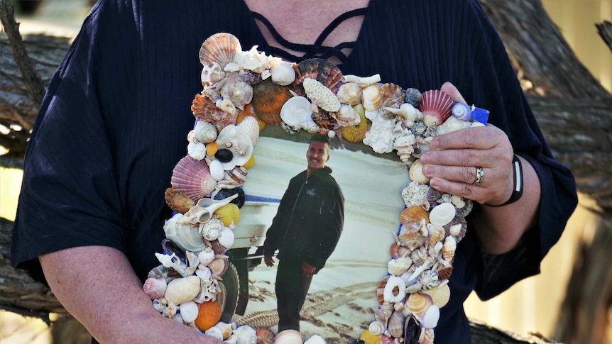 A picture frame containing a smiling photo of Damian Noakes on a beach.