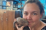 a woman holds a lizard and smiles at the camera.
