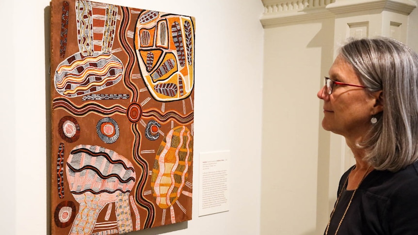 A woman stands in front of an Aboriginal artwork hanging on a wall