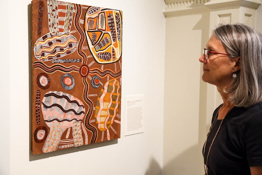 A woman stands in front of an Aboriginal artwork hanging on a wall