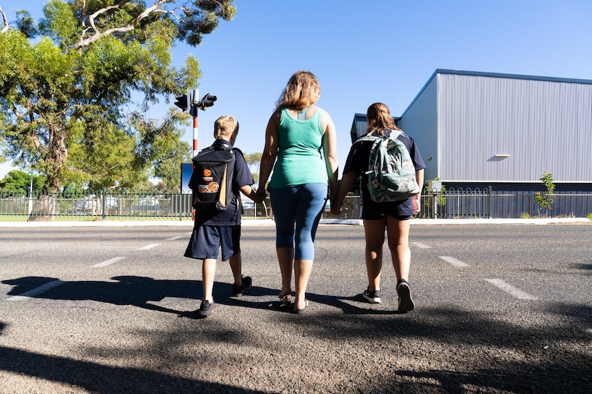 A woman walks towards a school holding the hands of her two children