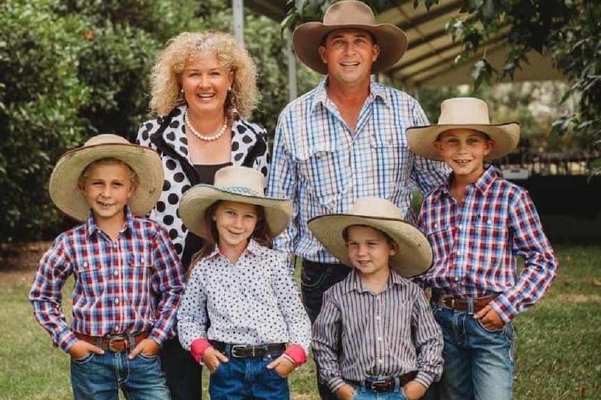 A man, woman and four kids standing outside. Most in wide brim hats, jeans and check shirts.