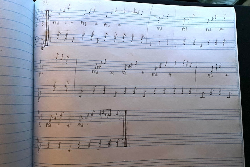 An open notebook with a musical composition written in pencil on a lined page.