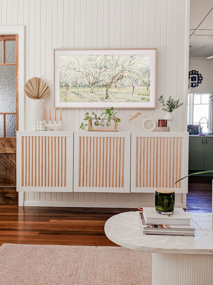 Three white and peach cabinets sits against a white panelled wall in a living room.