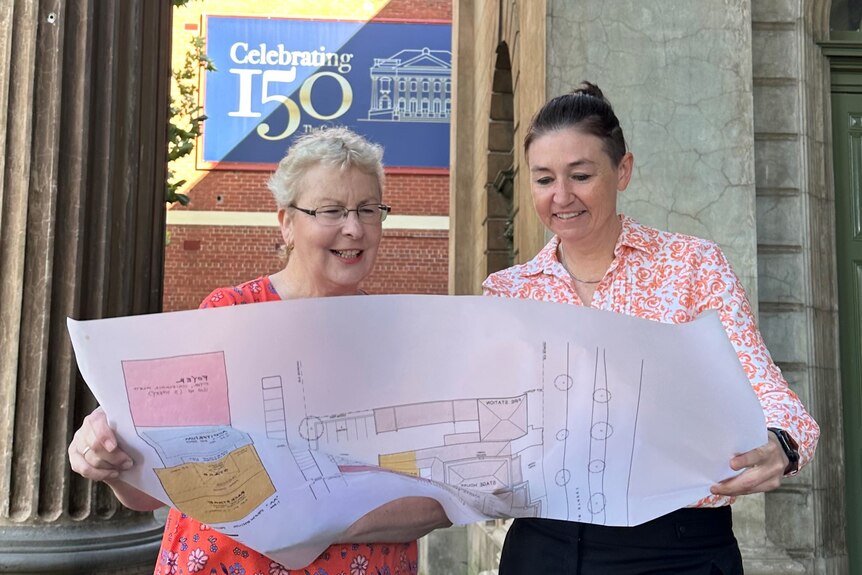 Two people looking at plans for a building, out the front of a sign celebrating 150 years of the Capital Theatre