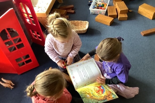 group of three children reading on floor of kindergarten