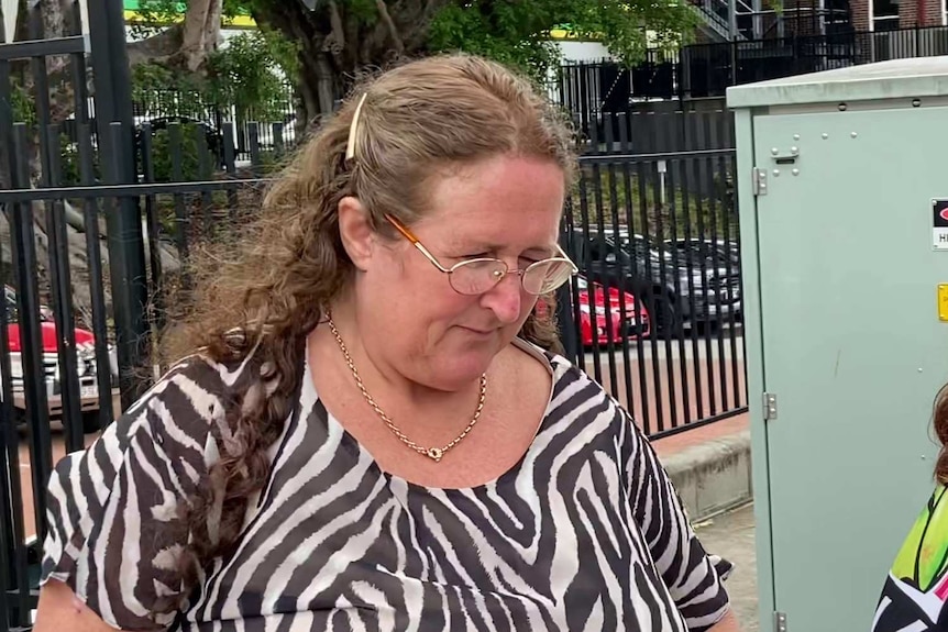 A woman in a zebra print shirt and glasses walks with her head down.