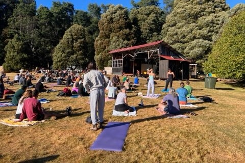 Festival goers sit on the grass in front of a stage.