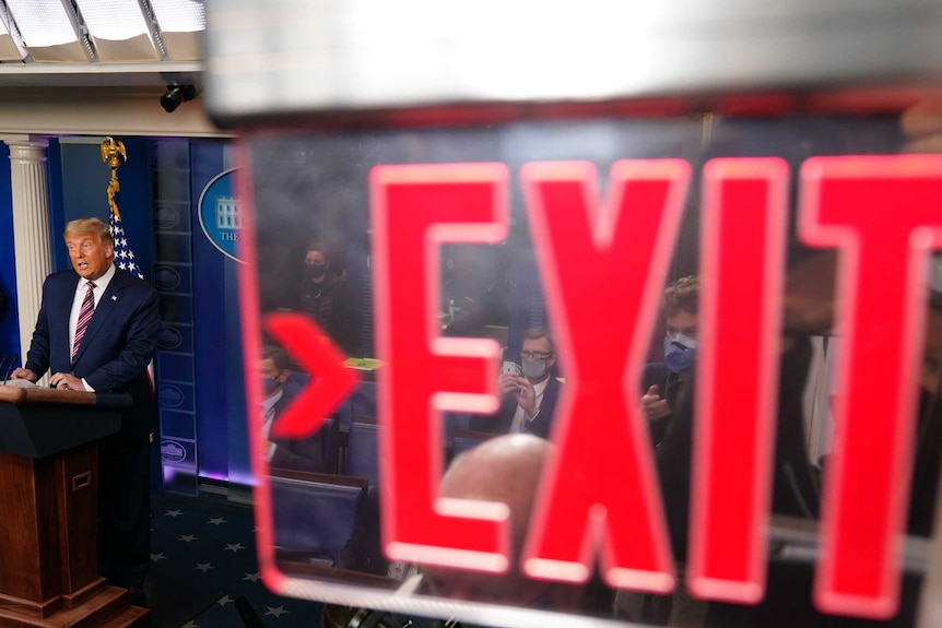 US President Donald Trump speaks next to an exit sign.