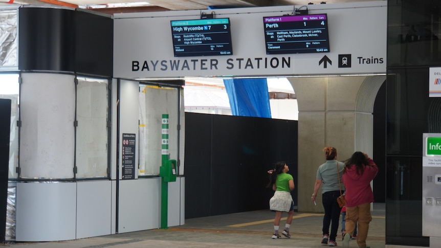 People walk beneath a Bayswater station sign