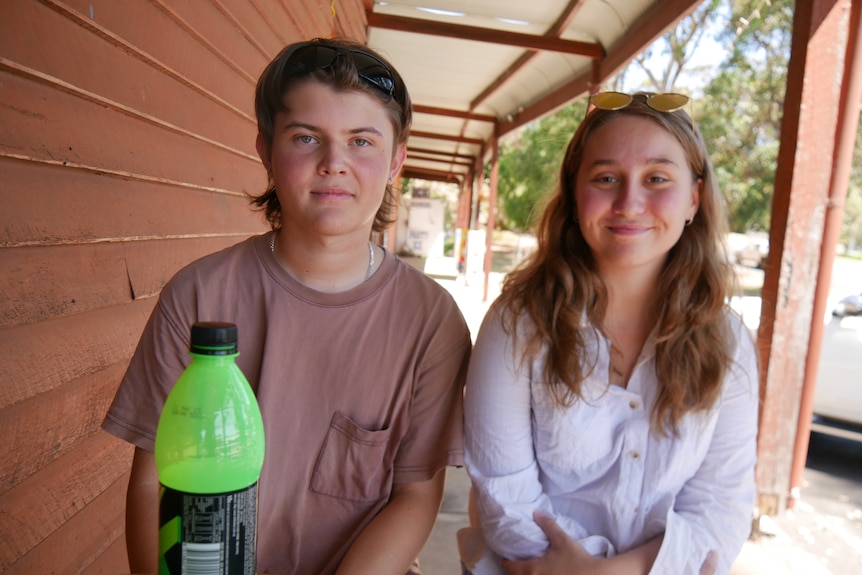 two young people sit at a table with a bottle of energy drink in front of them. 