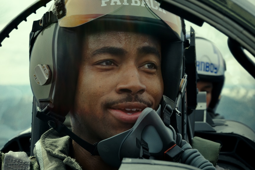 Close up on Black man with bemused expression wearing pilot headgear in a fighter jet.
