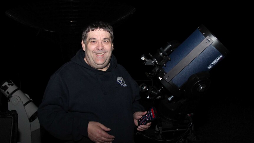 Man smiling next to a telescope