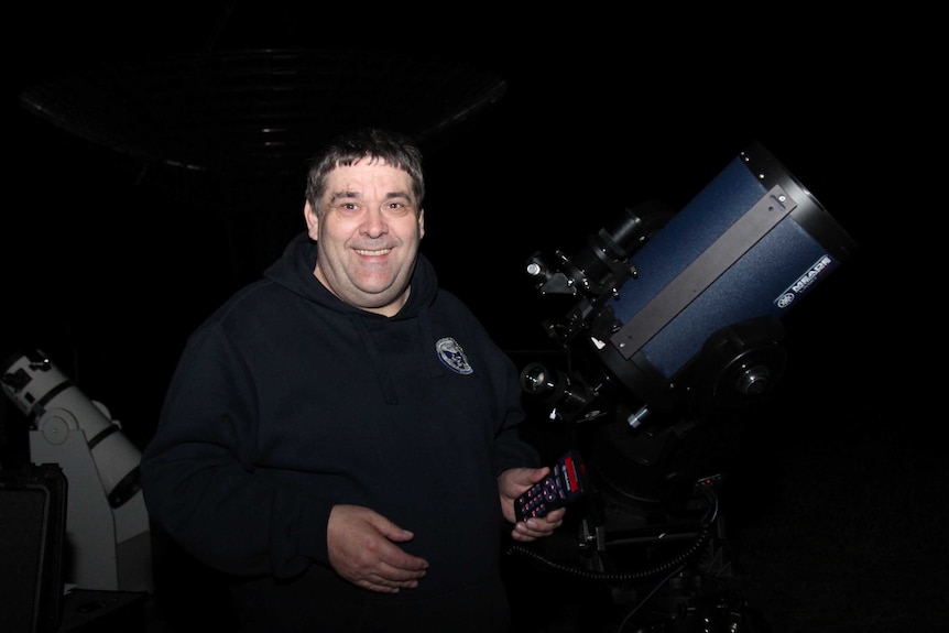 Man smiling next to a telescope