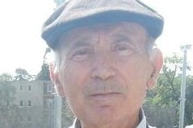 Theo Makridis, an elderly man wearing a hat, looks calmly at the camera.