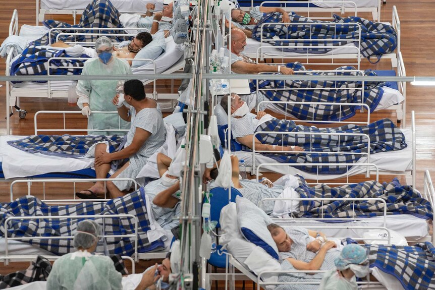 People lie on hospital beds on a wooden floor surrounded by medical staff wearing masks