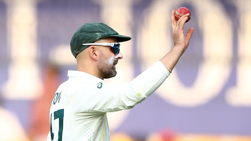 Nathan Lyon holds up a red cricket ball